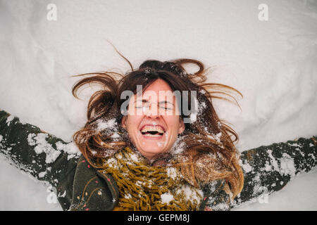 Una donna sdraiata su un banco di neve con le braccia tese. Foto Stock