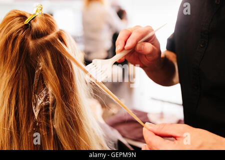 Un capello colorista, un uomo con un pennello per coprire le sezioni di una donna di capelli biondi. Foto Stock