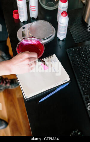 Un colorista di miscelazione di colorante per capelli utilizzando polvere e acqua, e test del colore su carta. Foto Stock