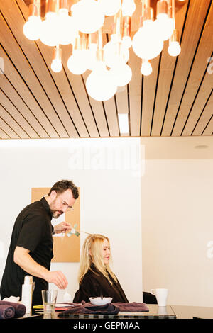Un capello colorista lavora con lamelle per dare un client con lunghi capelli biondi evidenzia e lowlights utilizzando il colore. Foto Stock