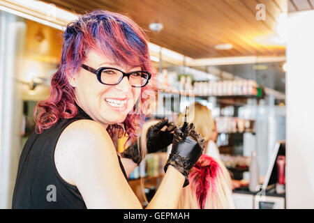 Un capello colorista guanti in applicazione di rosso colorante per capelli per un cliente del pelo biondo con un pennello. Foto Stock