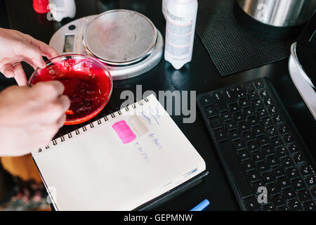 Un colorista di miscelazione di colorante per capelli utilizzando polvere e acqua, e test del colore su carta. Foto Stock