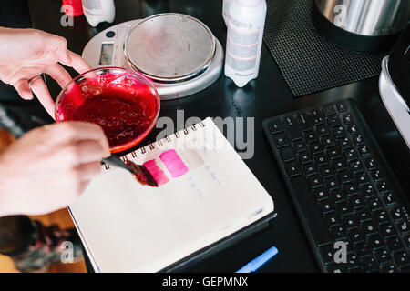 Un colorista di miscelazione di colorante per capelli utilizzando polvere e acqua, e test del colore su carta. Foto Stock