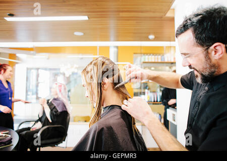 Un parrucchiere con un client, pettinando i suoi lunghi capelli in sezioni. Foto Stock