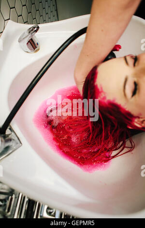 Un parrucchiere cliente avente rosso colorante per capelli lavati da i suoi capelli su un bacino. Foto Stock