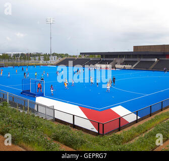 Campo di hockey su prato in blu con i giocatori. Eton Manor - Lee Valley Hockey e il Centro Tennis, Londra, Regno Unito. Architetto: Stanton Foto Stock