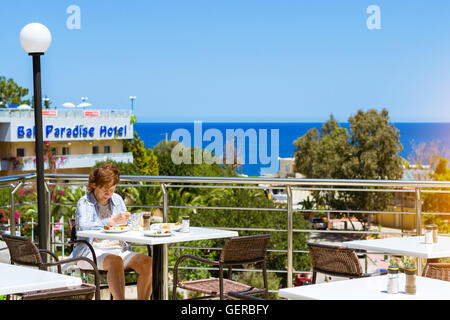 BALI, Grecia - 28 Aprile 2016: donna anziana in maglietta blu è a pranzo sulla veranda del ristorante, affacciato sul mare di Creta Foto Stock