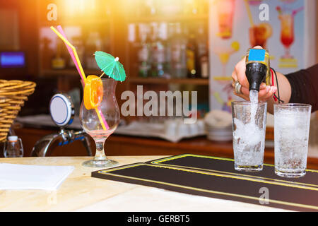 Bicchiere vuoto da cocktail con ombrellone, paglia e fetta di arancia è il bar al cafe'. Il barista versa la soda in bicchieri di ghiaccio Foto Stock