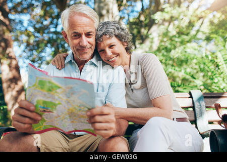 Paio di turismo maturo su una vacanza. Donna che comprenda l'uomo in possesso di una mappa. Felice coppia senior relax su una panchina nel parco la lettura Foto Stock