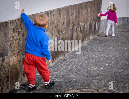 Bambini piccoli - fratello e sorella a piedi lungo la parete di casa in Spagna Foto Stock