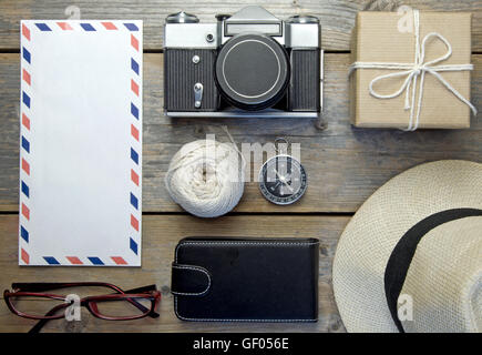 Piano di viaggio lay, fotocamera, Busta, cappello e bussola su un sfondo di legno Foto Stock