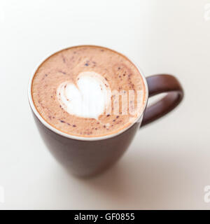 Tazza di caffè cappuccino con la schiuma di latte sulla parte superiore a forma di cuore, visto dal di sopra in una tazza marrone sul tavolo bianco Foto Stock