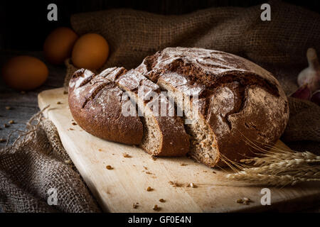 Pasta madre pane di segale affettato sul tagliere di legno. Rustico ancora in vita. Luce naturale, chiave di basso Foto Stock