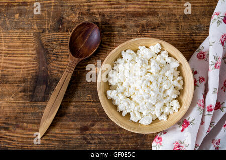 Cottage cheese (agricoltori formaggio) nella ciotola di legno, il cucchiaio di legno, tessile su tavola in legno rustico. Vista superiore del cibo. Mangiare sano Foto Stock