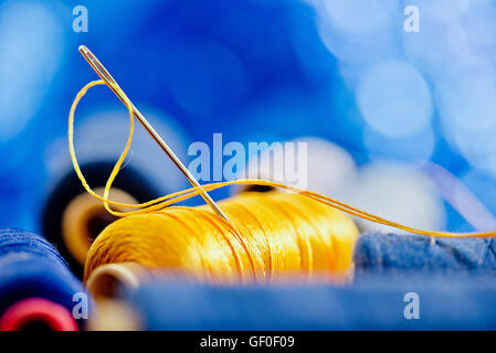 Ago e filo di colore giallo su sfondo blu Foto Stock