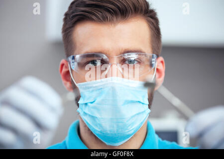 Dentista in maschera e occhiali di protezione pronto per iniziare a dental checkup. Foto Stock