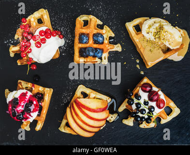 Belga caldo waffles fatti in casa con giardino fresco di bacche e frutta e gelato su ardesia scura sullo sfondo di pietra Foto Stock