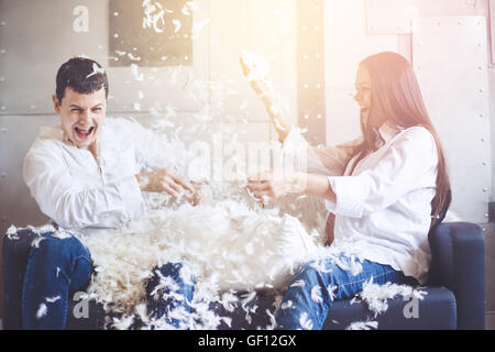 Pillow Fight. Giovani felice famiglia incinta divertirsi con piume soffici dal cuscino. L uomo e la donna vestita in jeans e bianco sh Foto Stock