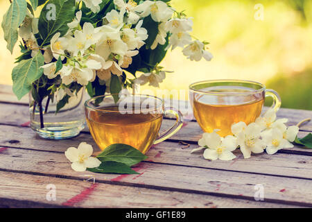 Due tazze di tè verde con fiori di gelsomino su grunge tavolo in legno nel giardino Foto Stock