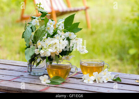 Due tazze di tè verde con fiori di gelsomino su grunge tavolo in legno nel giardino Foto Stock