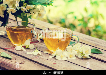 Due tazze di tè verde con fiori di gelsomino su grunge tavolo in legno nel giardino Foto Stock