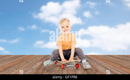 Felice piccolo ragazzo seduto su skateboard Foto Stock