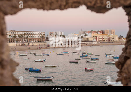 Vista La Caleta Beach, visto attraverso i bastioni del Castillo de Santa Catalina fortezza, al tramonto. La Caleta è un piccolo Foto Stock