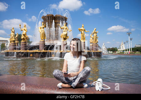 Giovane bella donna ha un resto seduta vicino alla Fontana di amicizia del popolo vista giornaliera a VDNH mostra a Mosca, Foto Stock