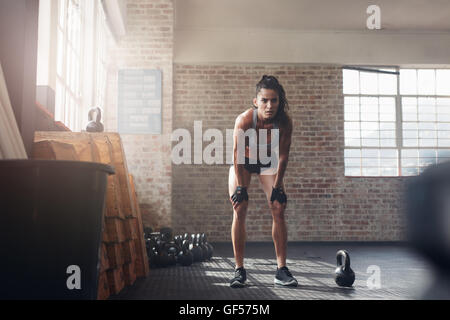 A piena lunghezza shot di fiducioso giovane donna alla palestra crossfit. Sportive muscolare in piedi con le mani sulle ginocchia cercando focalizzata Foto Stock