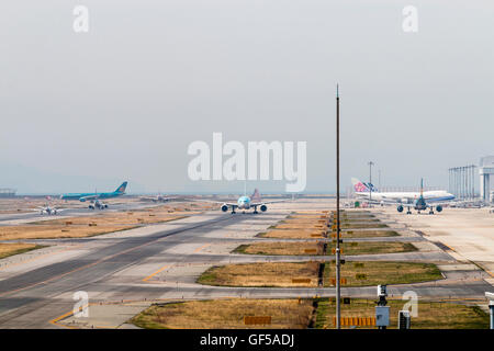 Giappone, Osaka Kansai, Aeroporto KIX. "KLM Asia' 777-206ER rullaggio sulla pista. Un altro aeromobile rullaggio lungo grembiule. Visto attraverso il calore haze. Foto Stock