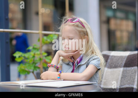 Adorabili bambini menu di lettura nella caffetteria. Il Toddler stanco ragazza in bella fuori café pasto scegliendo dal menu Scheda. Foto Stock