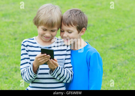 I bambini con il cellulare all'aperto. Due ragazzi sorridenti, cercando di schermo, la riproduzione di giochi o utilizzando l'applicazione. Tecnologia istruzione tempo libero concetto di persone Foto Stock