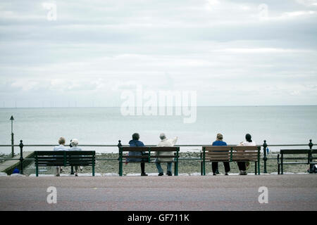 La gente seduta sulla promenade panche affacciato sulla marea a Llandduno, Wales, Regno Unito Foto Stock