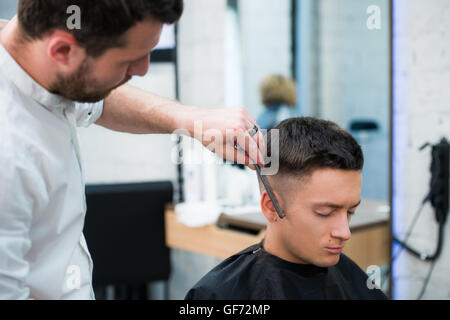 Ritratto di uomo bello con i capelli neri con taglio di capelli al salone. Parrucchiere tenendo il pettine e forbici. Foto Stock