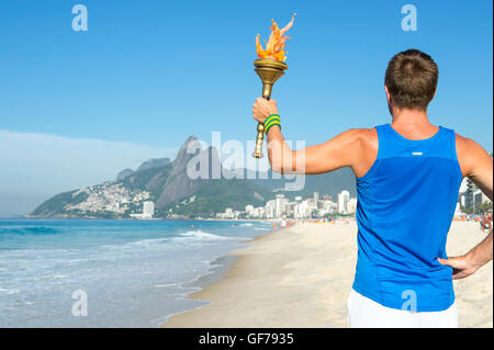 Torchbearer atleta in piedi con sport torcia sopra il Rio de Janeiro, Brasile skyline a Ipanema Beach Foto Stock