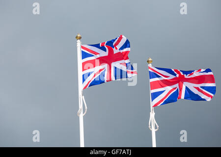 Due Union Jack Flag su pali di bandiera che soffia nella brezza contro tempestoso cieli grigi a Dorset in luglio Foto Stock
