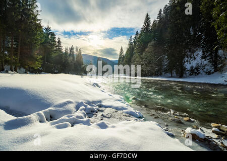 Frozen River tra foreste di conifere con neve sul terreno nelle montagne dei Carpazi Foto Stock