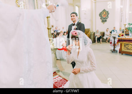 Sposa prega sulle ginocchia in piedi nella parte anteriore del sacerdote nella chiesa Foto Stock