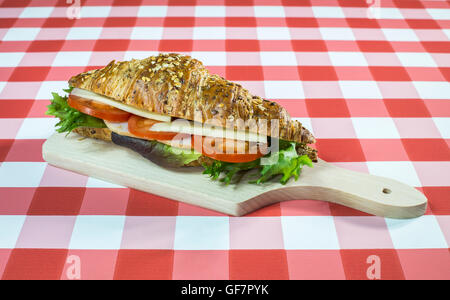 Squallido sandwich croissant su una tovaglia a scacchi. Foto Stock