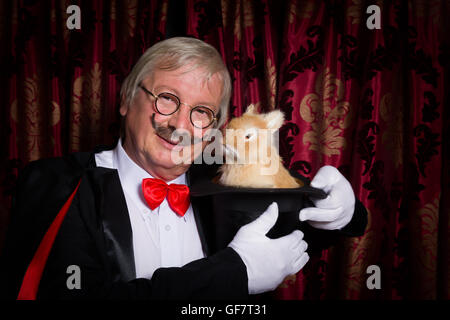 Funny illusionista sul palco con un coniglio nel suo top hat Foto Stock