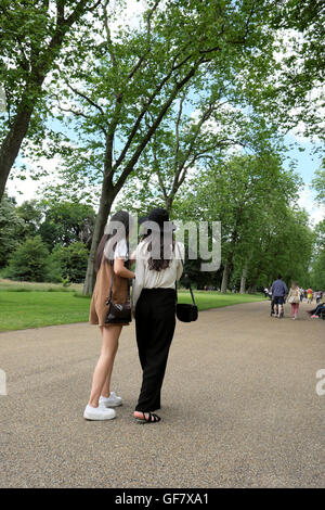 Vista posteriore di 2 Asia le giovani donne a piedi lungo un sentiero in estate 2016 Hyde Park, Londra UK KATHY DEWITT Foto Stock