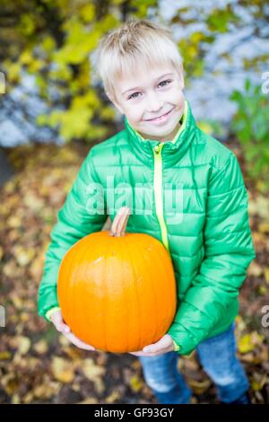 Modello rilasciato. Ragazzo biondo tenendo la zucca nel parco, ritratto, sorridente. Foto Stock