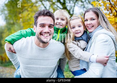 Modello rilasciato. I genitori che trasportano i loro figli in autunno, ritratto, sorridente. Foto Stock