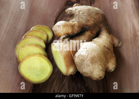 Radice di Zenzero intero e tagliata a fette, disposte su un piano di legno. Foto Stock