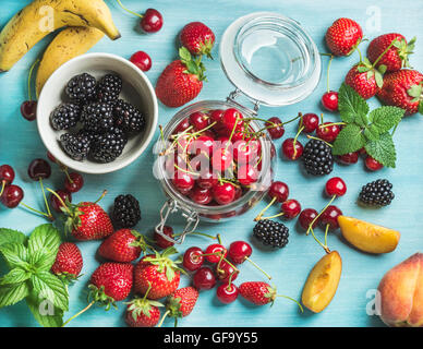 Una sana frutta estiva varietà. Ciliegie dolci, fragole, more, le pesche, le banane e le foglie di menta su sfondo blu Foto Stock