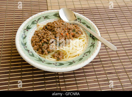 Spaghetti nella ciotola con il sugo di carne e il cucchiaio sul tappetino di bambù Foto Stock