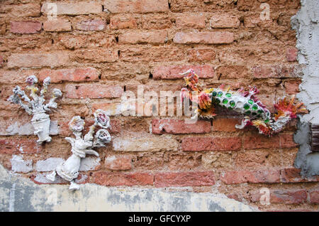 La scultura dragon e fiore dal cemento su un muro di mattoni sullo sfondo di un antico edificio della parete in corrispondenza di arte di strada di George Town in Foto Stock