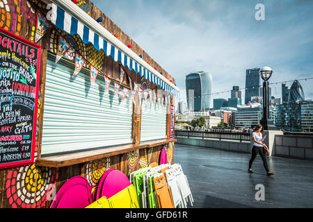 Una giovane donna cammina un passato brillantemente colorato cocktail bar accanto al fiume Tamigi su Queen's Walk, London, SE1, Regno Unito Foto Stock