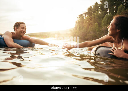 Affettuosa coppia giovane circa per tenere le mani mentre galleggiante su tubi interni in acqua. Giovane uomo e donna in un tubo gonfiabile Foto Stock