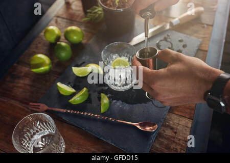 Primo piano delle mani di uomo versando la bevanda alcolica in un jigger per preparare un cocktail. Il barman prepara il cocktail al bar cou Foto Stock